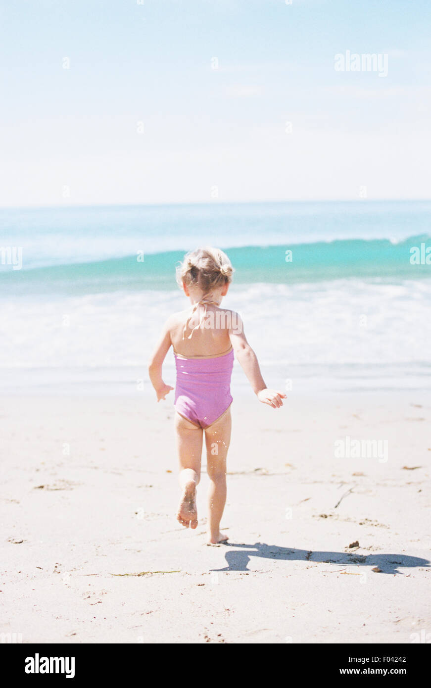 Jeune fille dans un maillot rose s'exécutant sur une plage de sable. Banque D'Images