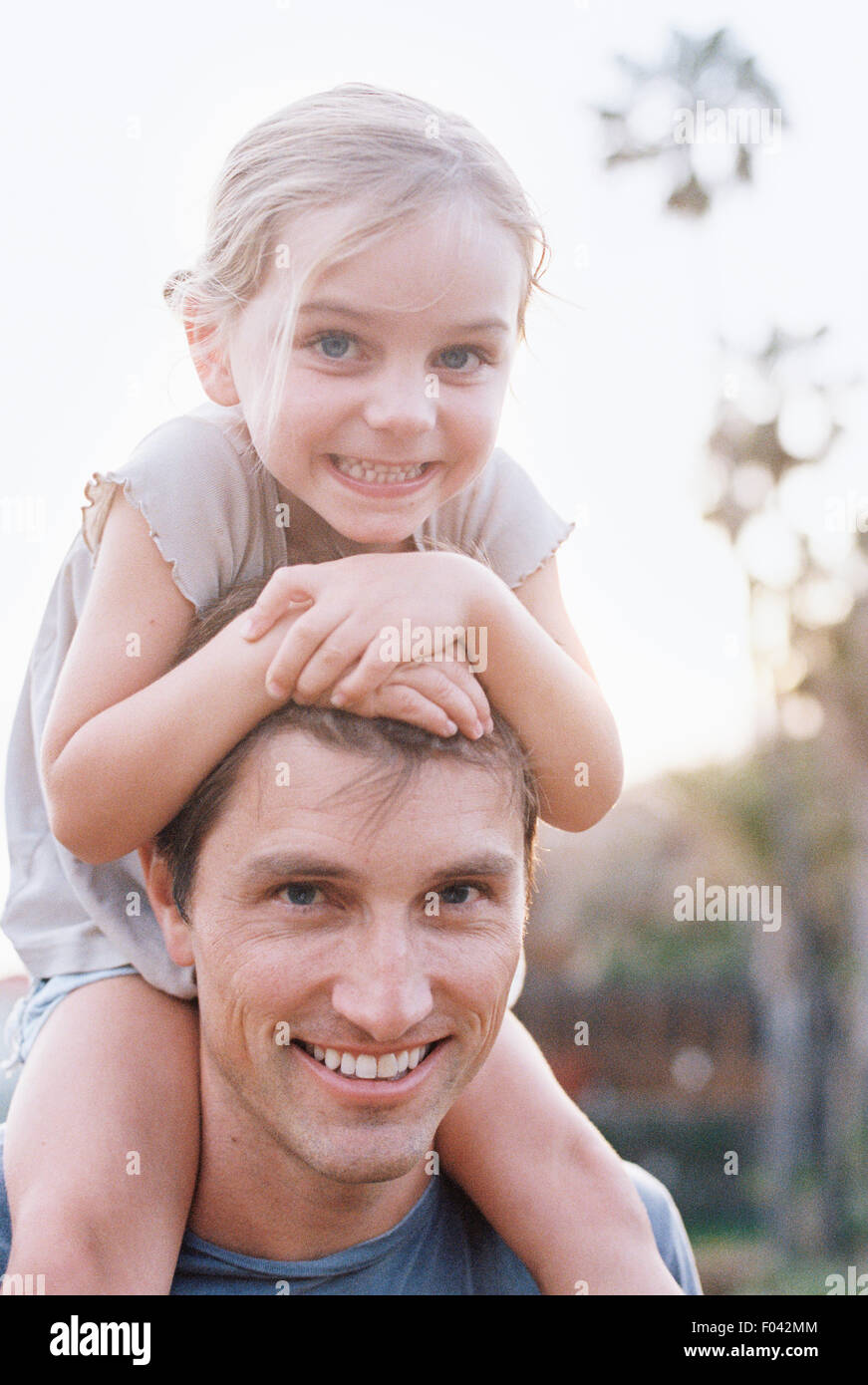 Un homme et sa fille souriant à l'appareil photo, l'enfant assis sur ses épaules. Banque D'Images