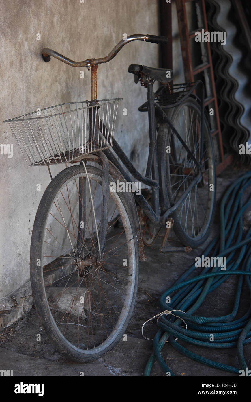 Un vieux vélo avec le panier, d'un flexible et d'autres outils de jardin dans la cour intérieure du village près du mur Banque D'Images