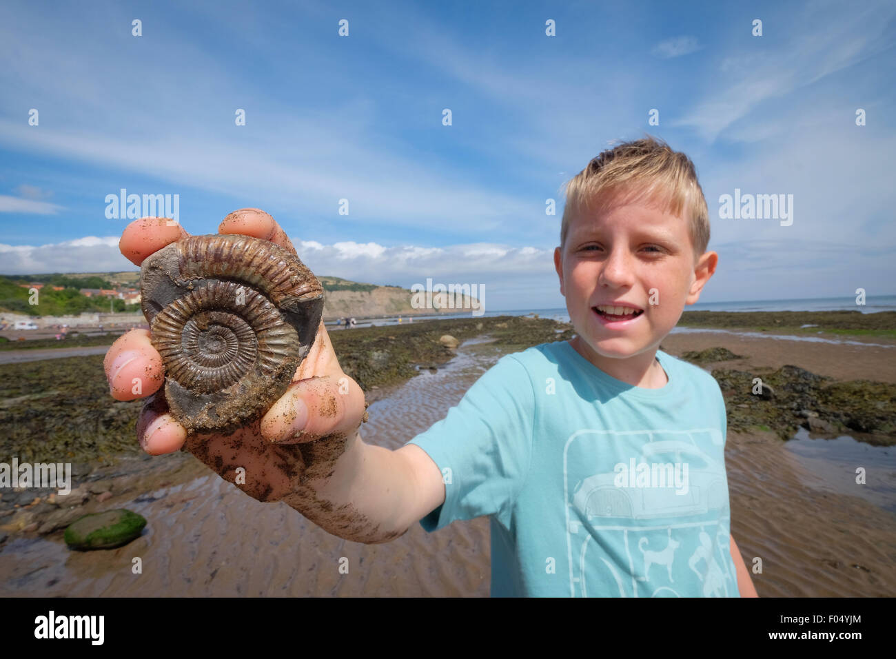 Un garçon avec un fossile d'ammonite sur la plage de Robin Hood's Bay, une partie de la côte jurassique du Yorkshire Banque D'Images