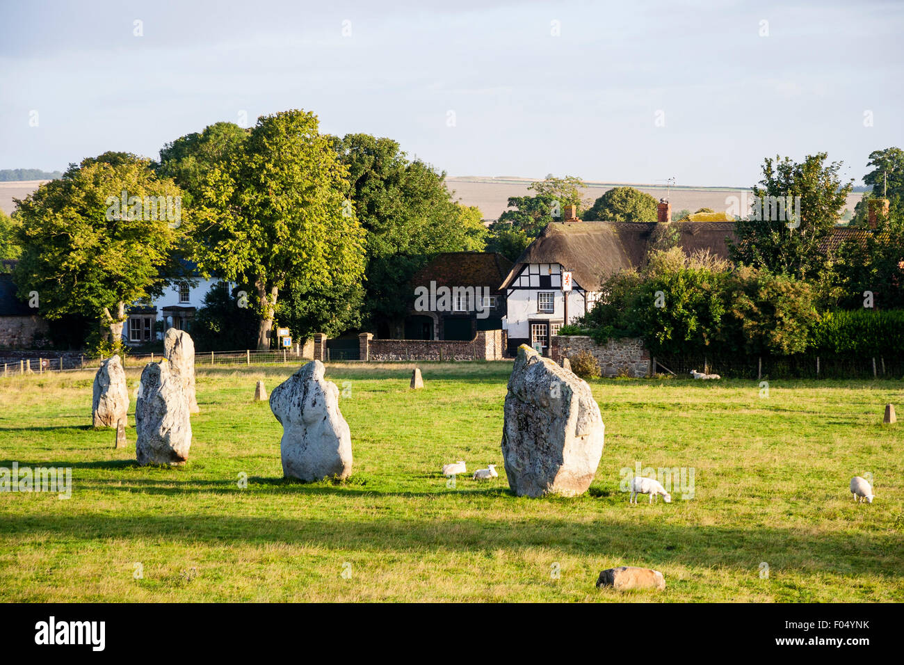 D'Avebury néolithique. Pierres du sud du cercle intérieur, avec arrière-plan de ferme de style Tudor et de ciel bleu. Banque D'Images