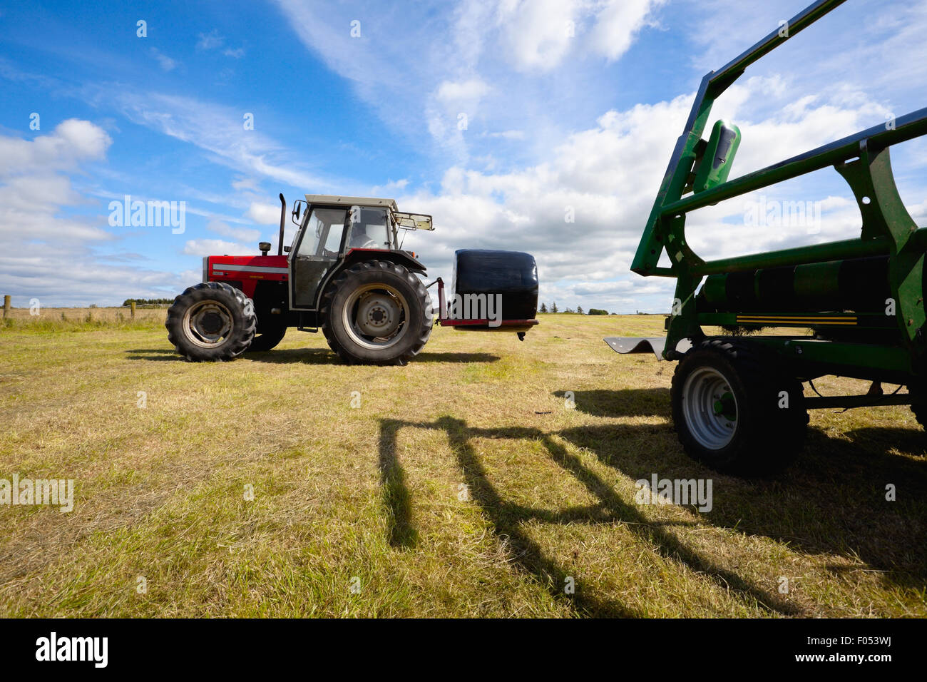 Tracteur énorme la collecte d'une botte de rouleau dans le champ à la belle journée ensoleillée bleu Banque D'Images