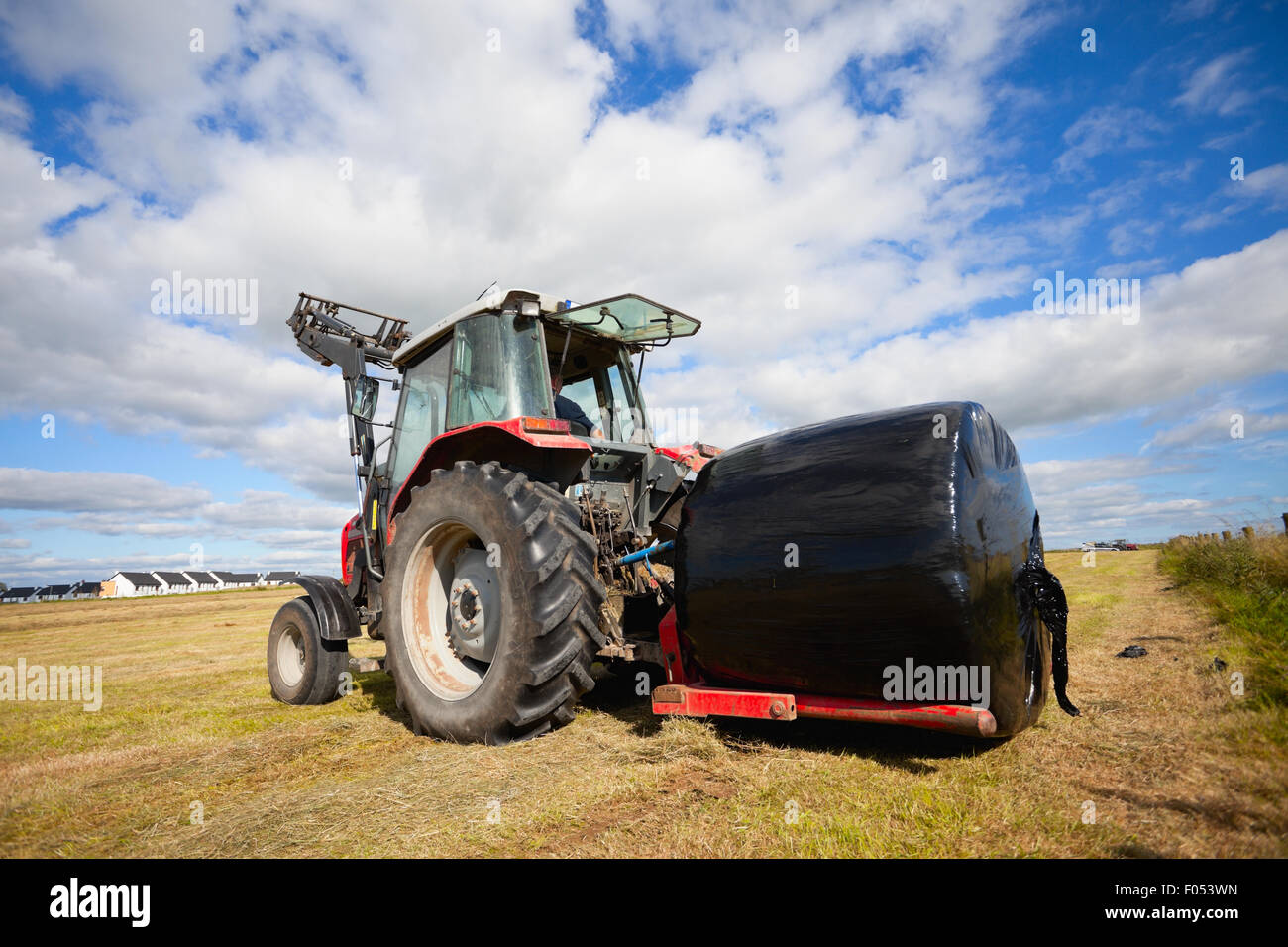 Tracteur énorme la collecte d'une botte de rouleau dans le champ d'une belle journée ensoleillée bleu Banque D'Images