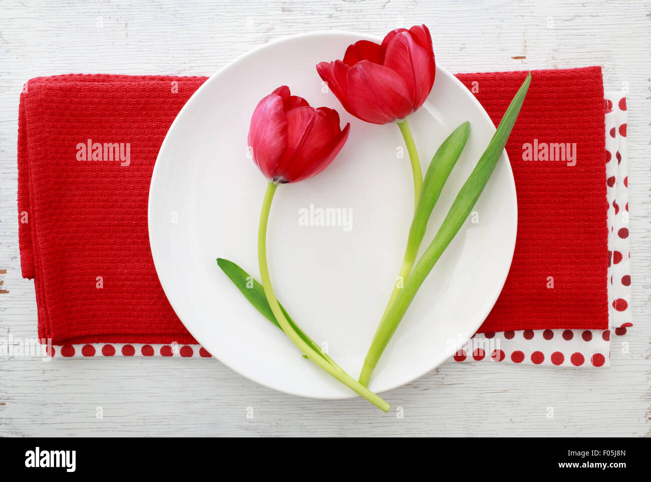 Deux tulipes rouges sur la plaque blanche sur des serviettes de table rouge Banque D'Images