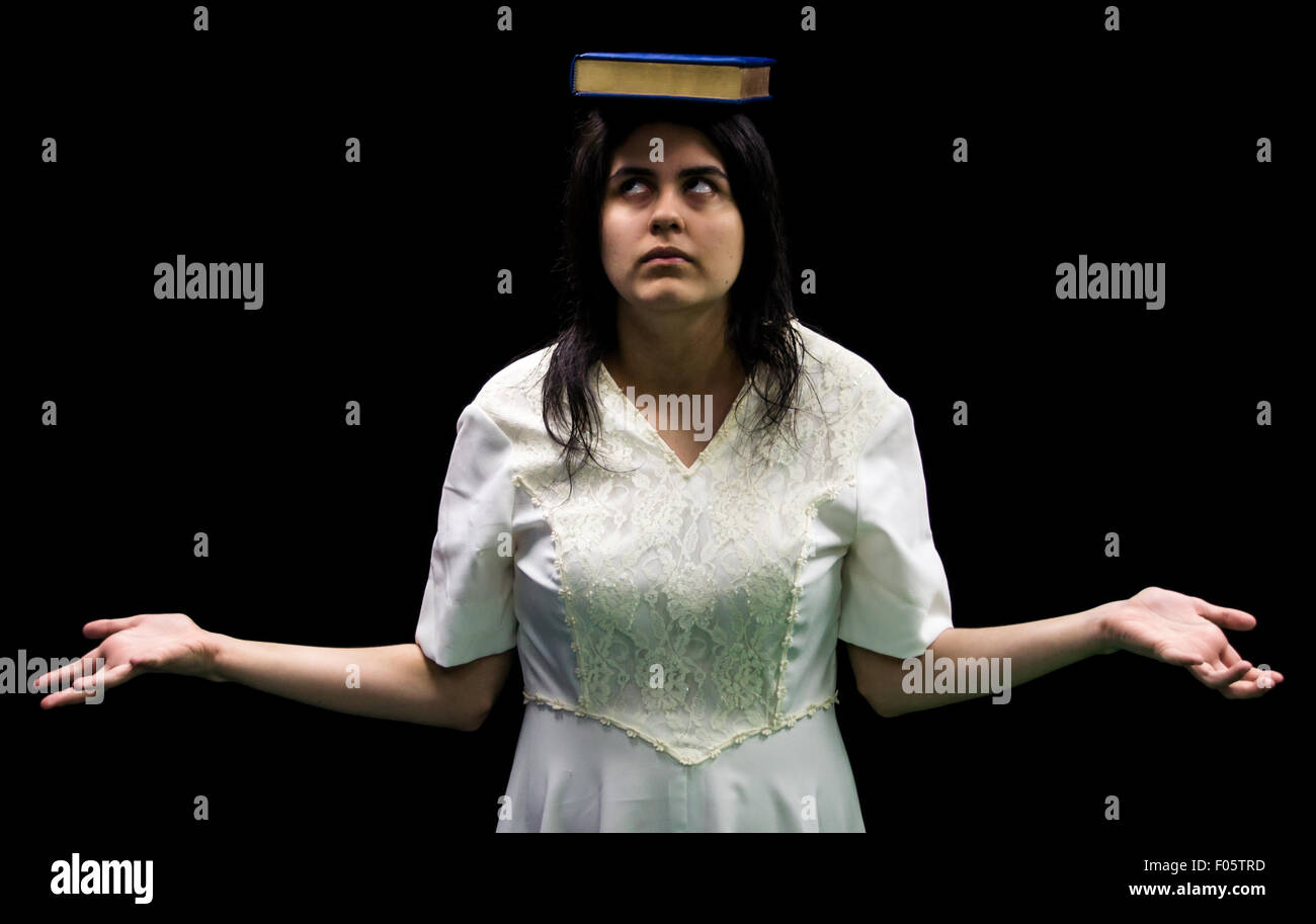 Latina adolescent en robe blanche debout devant fond noir Achat de livres sur la tête et levant les yeux Banque D'Images