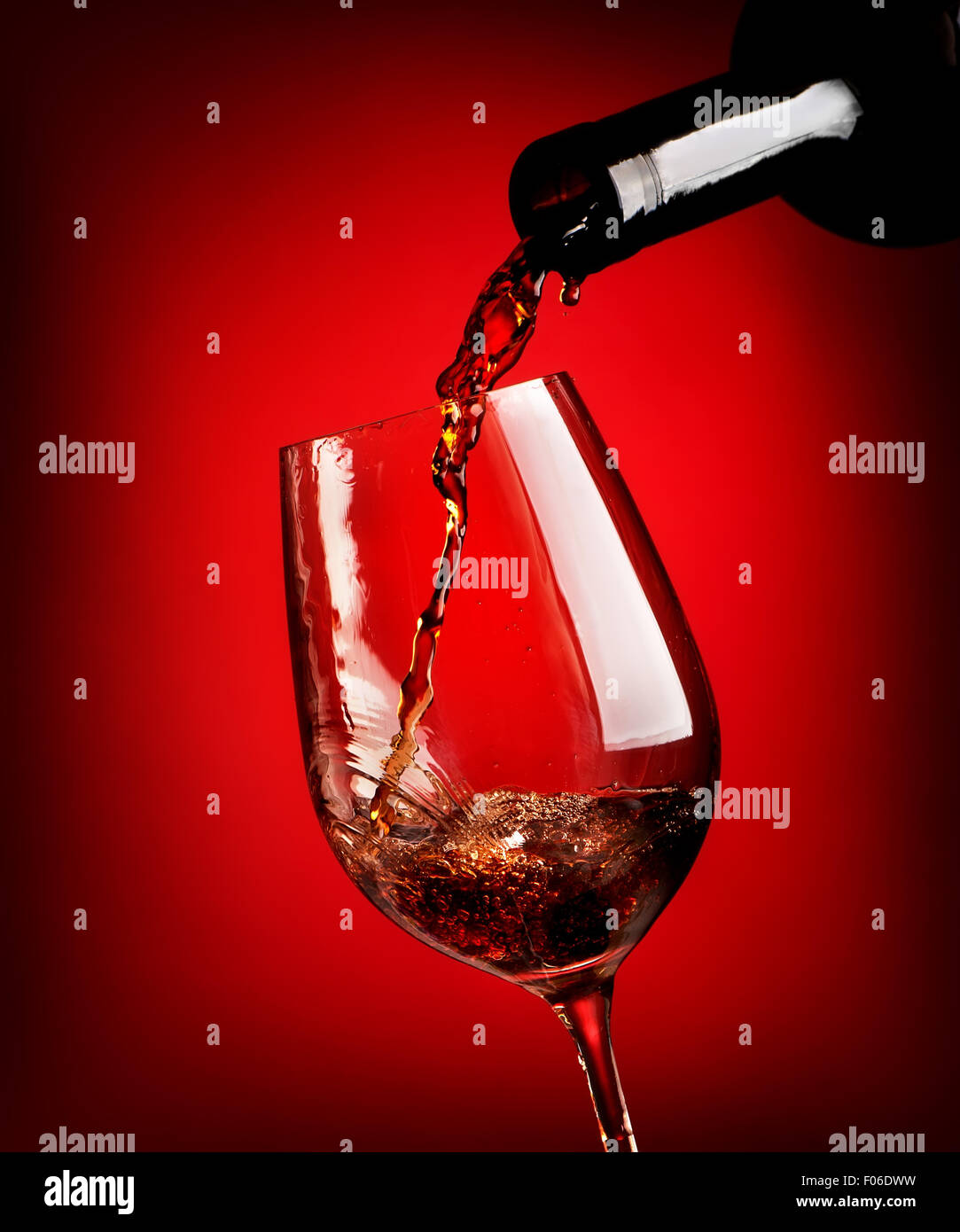 Verser le vin rouge dans un verre sur un fond rouge Banque D'Images
