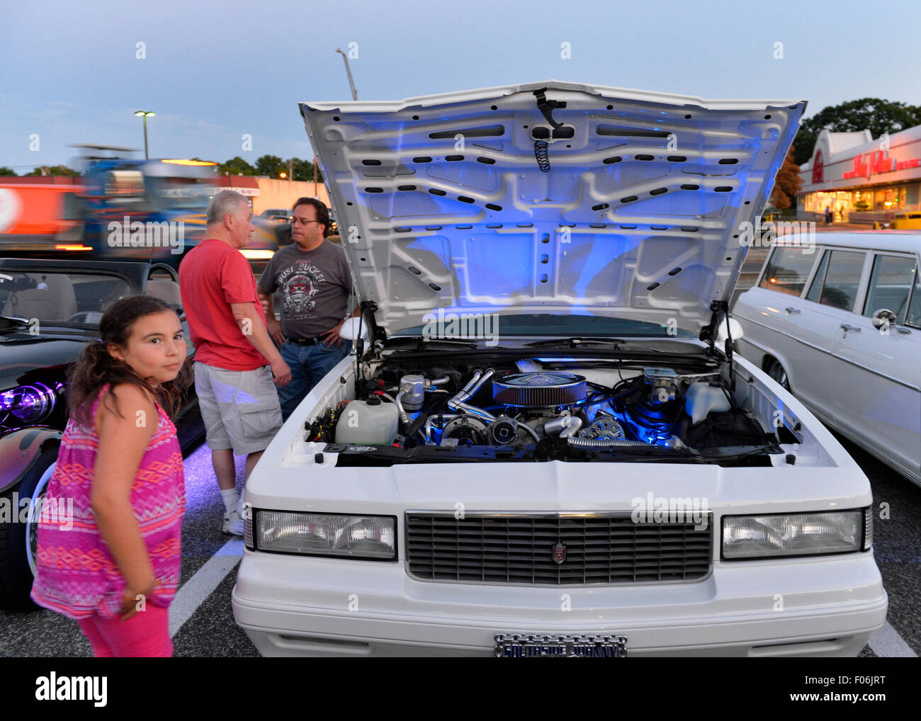 Bellmore, New York, USA. 7 août 2015. Une jeune fille et d'autres cherchent à white 1987 Chevy Monte Carlo, administré par Jean Gilson, de Islip, avec feux bleus sous capot, au vendredi soir Car Show s'est tenue à l'Bellmore Long Island Railroad Station Parking. Gilson a été l'un des nombreux membres de la South Side Boys auto club participant à la Nuit de Croisière. Des centaines de classique, antique, et les voitures personnalisées ont été à l'émission hebdomadaire libre, parrainé par la Chambre de Commerce de l'Bellmores. Banque D'Images