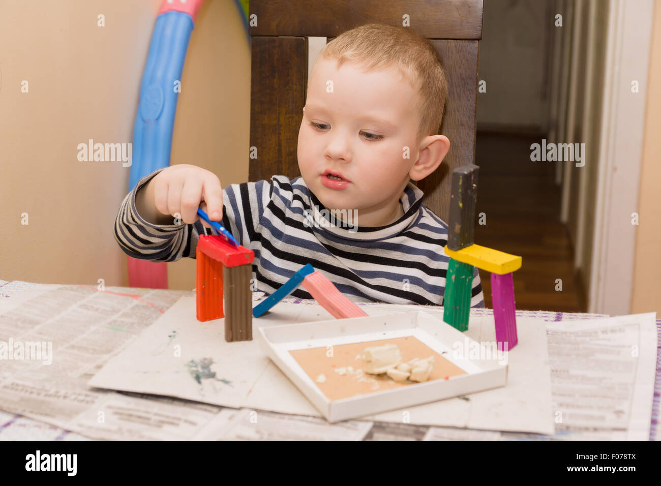 Le petit garçon est assis à une table et s'est engagé dans un moulage à partir de pâte à modeler Banque D'Images