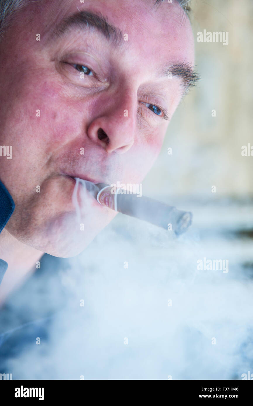 Un homme jouit d'un cigare et grimaces tout en fumeurs Banque D'Images