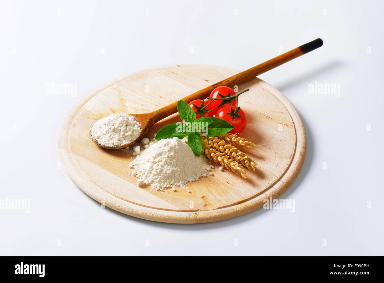 Tas de farine de blé tendre, cuillère en bois et tomates fraîches sur la planche à découper ronde Banque D'Images