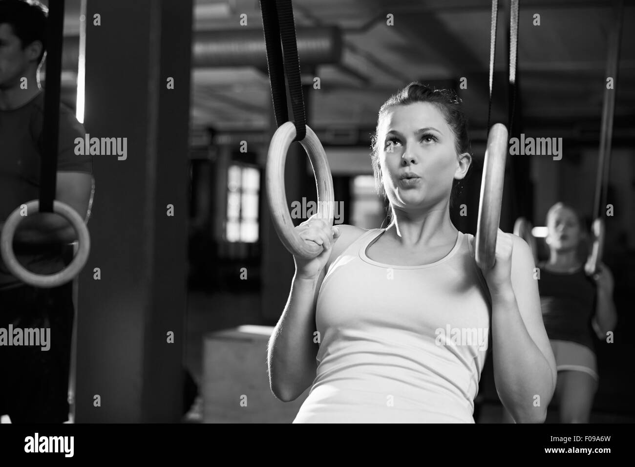 Tourné en noir et blanc d'une femme à l'aide d'anneaux de gymnastique en salle de sport Banque D'Images