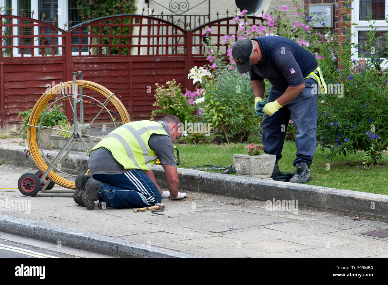 Les travailleurs de sexe masculin en câble d'alimentation pour connecter la chaussée d'une propriété résidentielle à large bande haute vitesse Banque D'Images