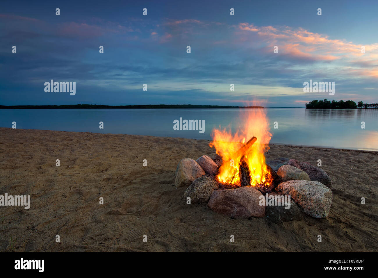 Feu de camp sur une plage de sable fin, à côté du lac au coucher du soleil. Banque D'Images