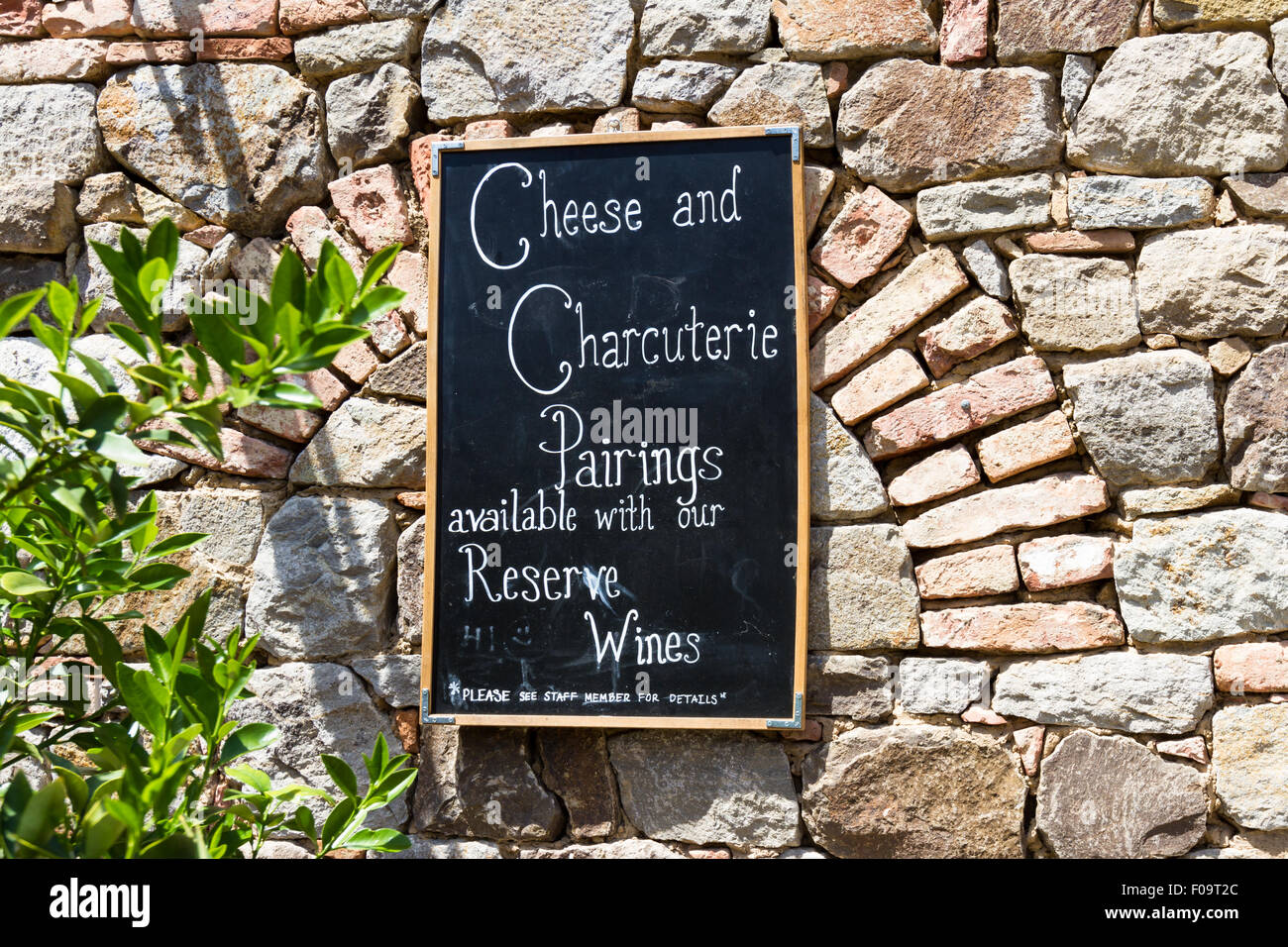 Un tableau noir sur un vieux mur de brique offrant le fromage et charcuterie avec vin Banque D'Images