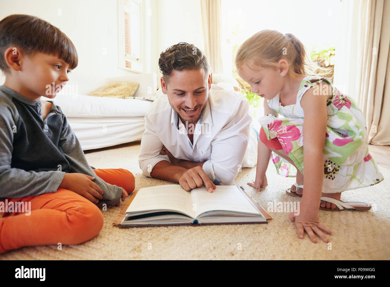 Famille la lecture d'un livre sur le plancher dans le salon. Père lire des histoires à son fils et de sa fille à la maison. Jeune homme, peu Banque D'Images