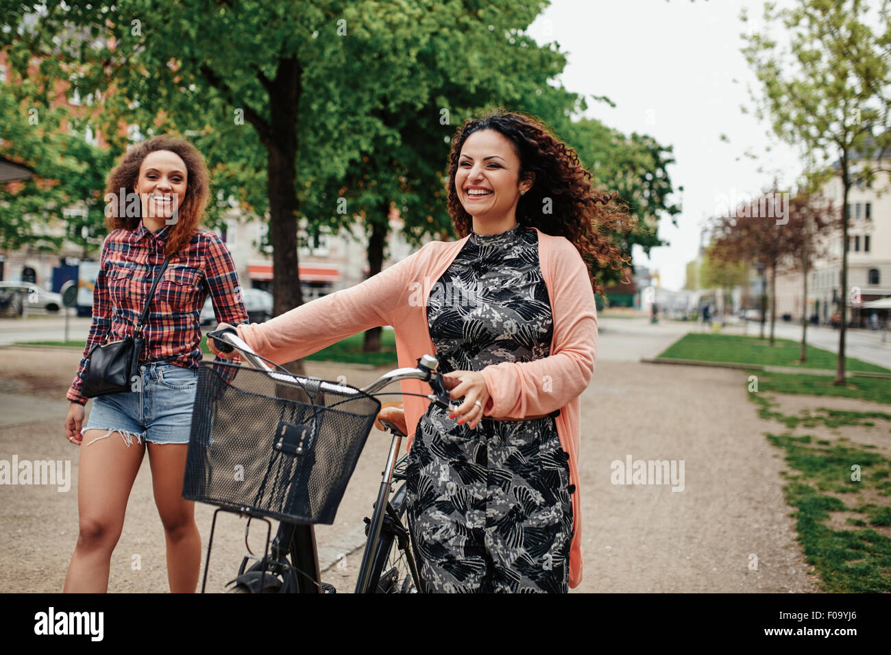 Souriante jeune amis marchant sur la rue de la ville, une femme pousse son vélo. Deux jeunes filles Hipster cycle avec ayant f Banque D'Images