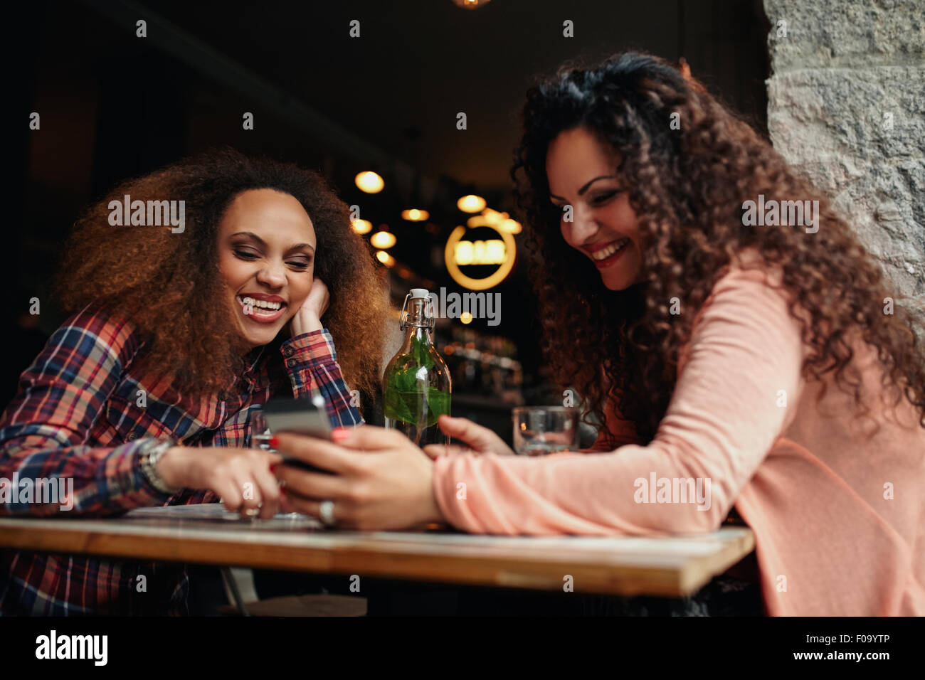 Deux jeunes femmes s'amuser ensemble, à l'aide d'un téléphone intelligent. Happy young female friends sitting together at cafe. Banque D'Images