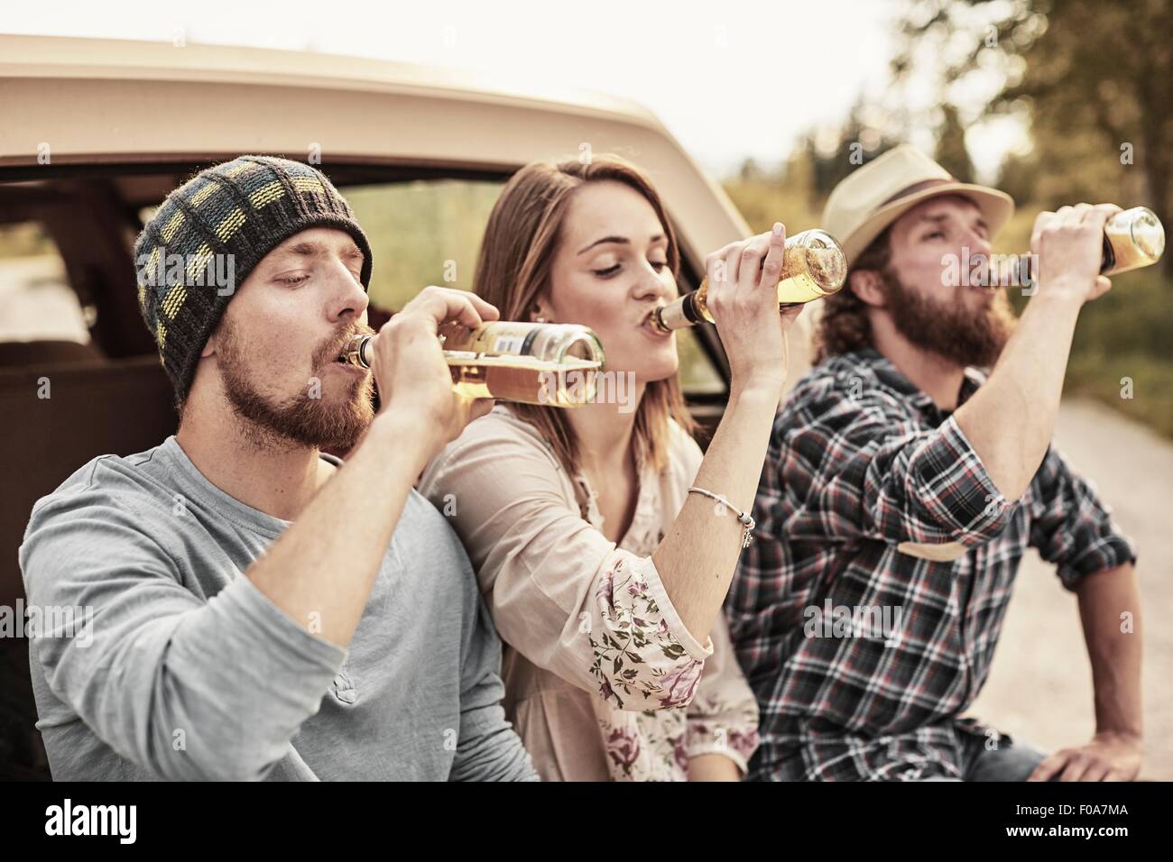 Trois personnes de boire la bière en bouteille à l'unisson Banque D'Images