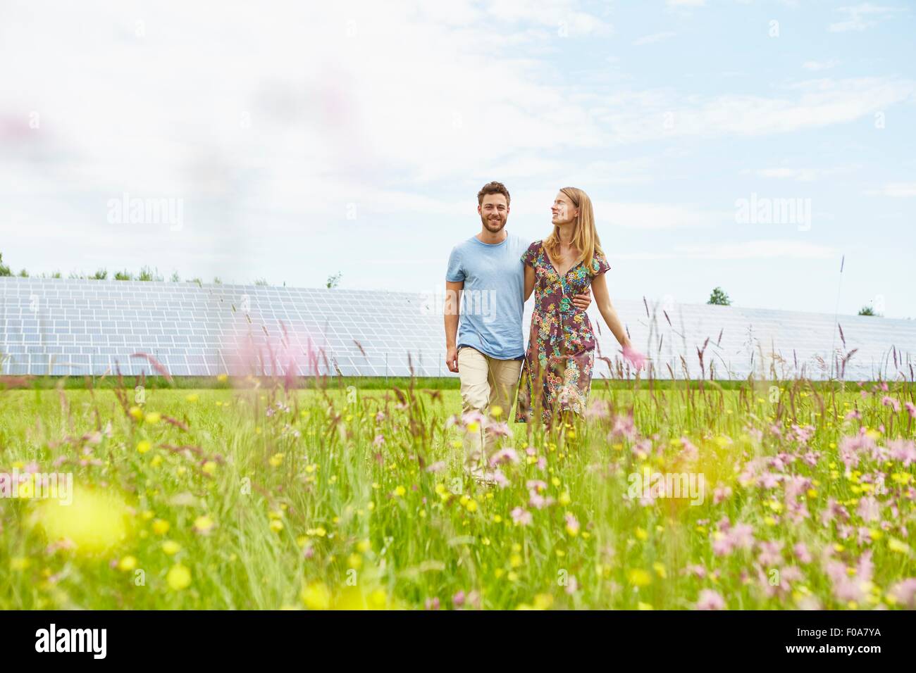 Jeune couple en train de marcher à travers champ en regard de la ferme solaire Banque D'Images