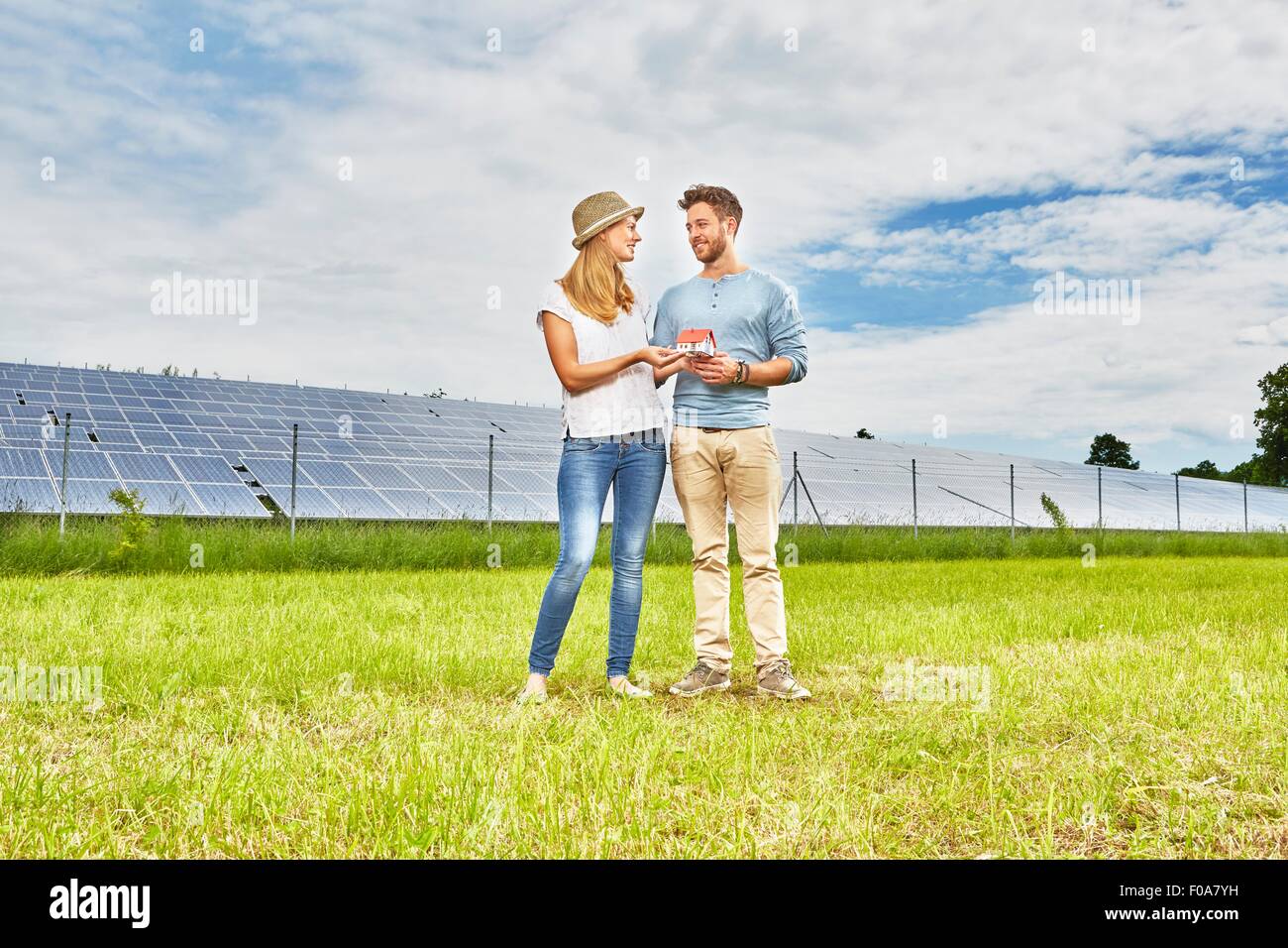 Jeune couple standing in field petit modèle de maison, à côté de la ferme solaire Banque D'Images