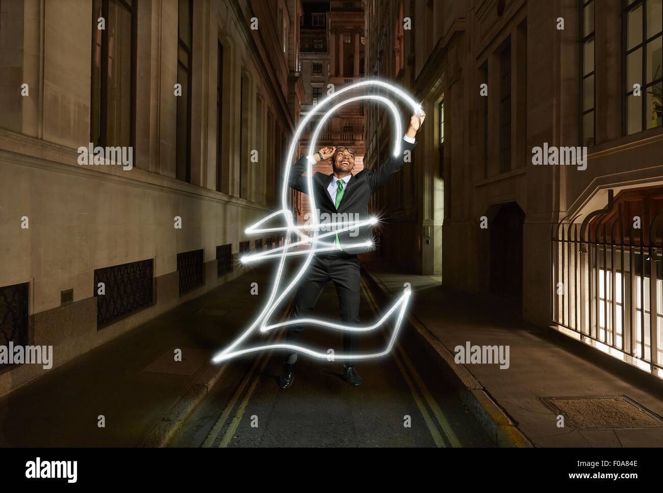 Young businessman light painting livre sterling symbole sur city street at night, London, UK Banque D'Images