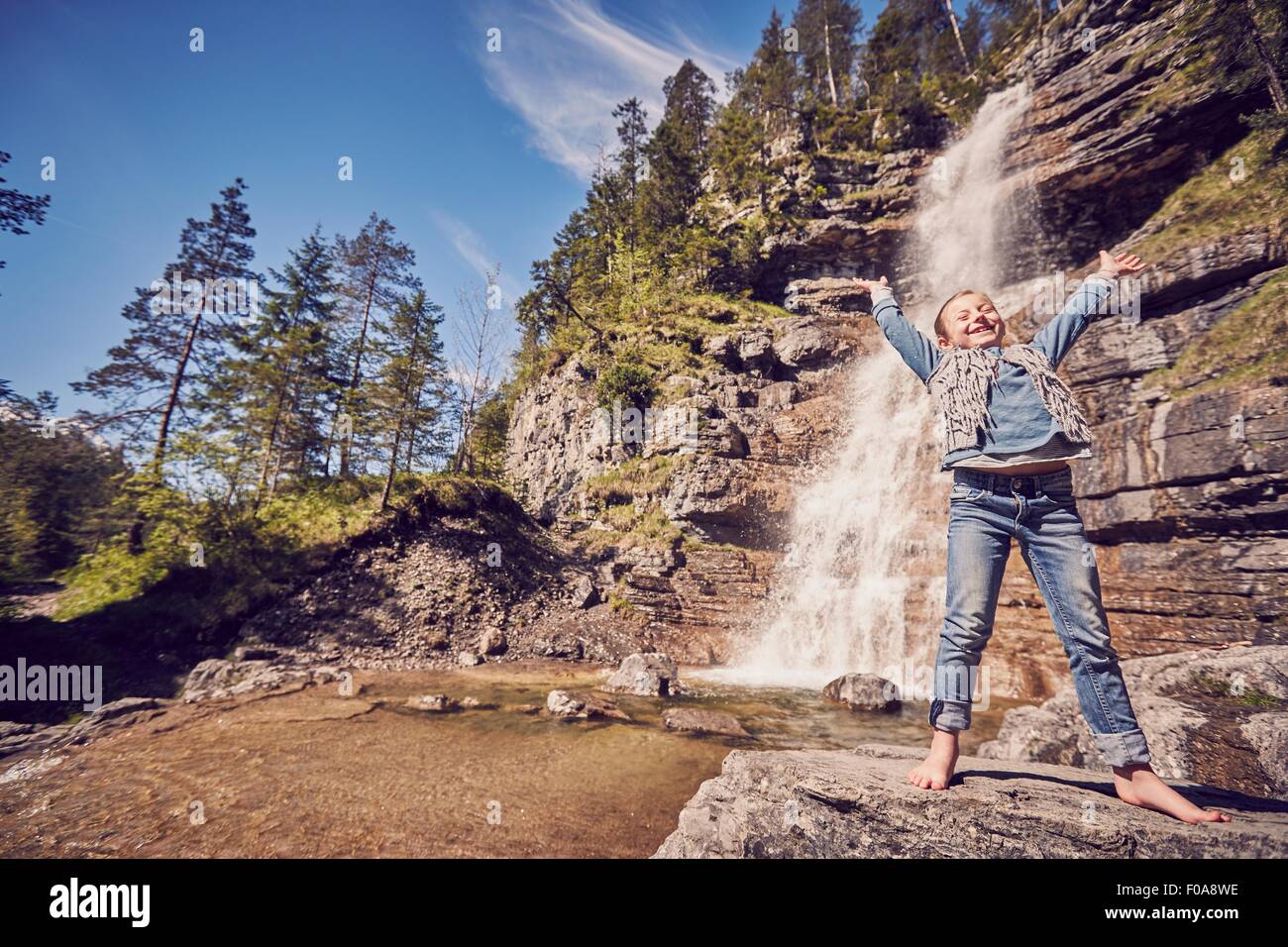 Jeune fille debout sur le rocher, à côté d'une cascade, bras levés dans l'excitation Banque D'Images