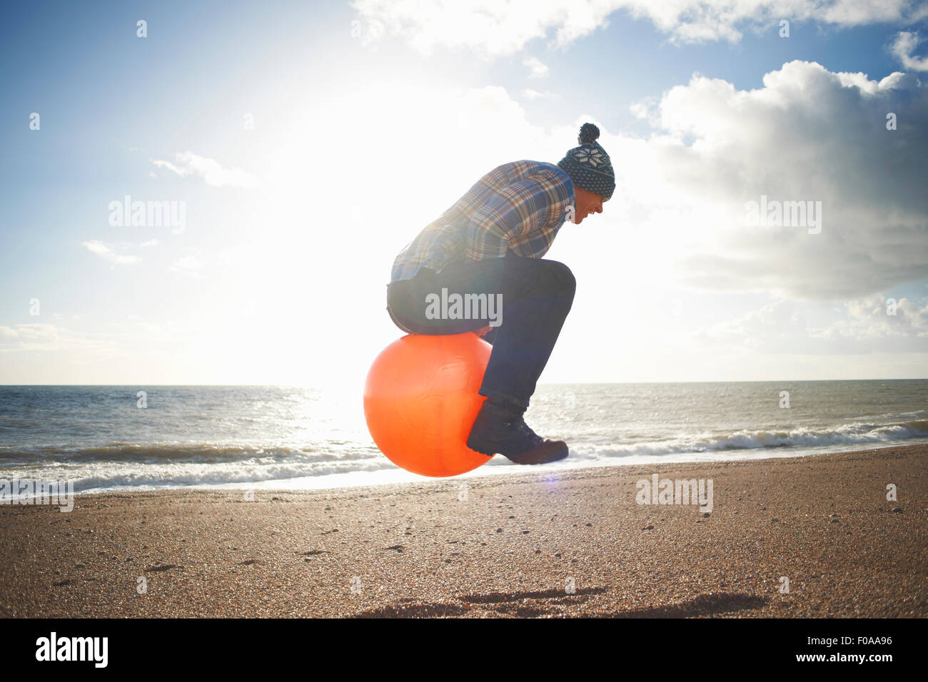 Man jumping mid air gonflable sur hopper at beach Banque D'Images