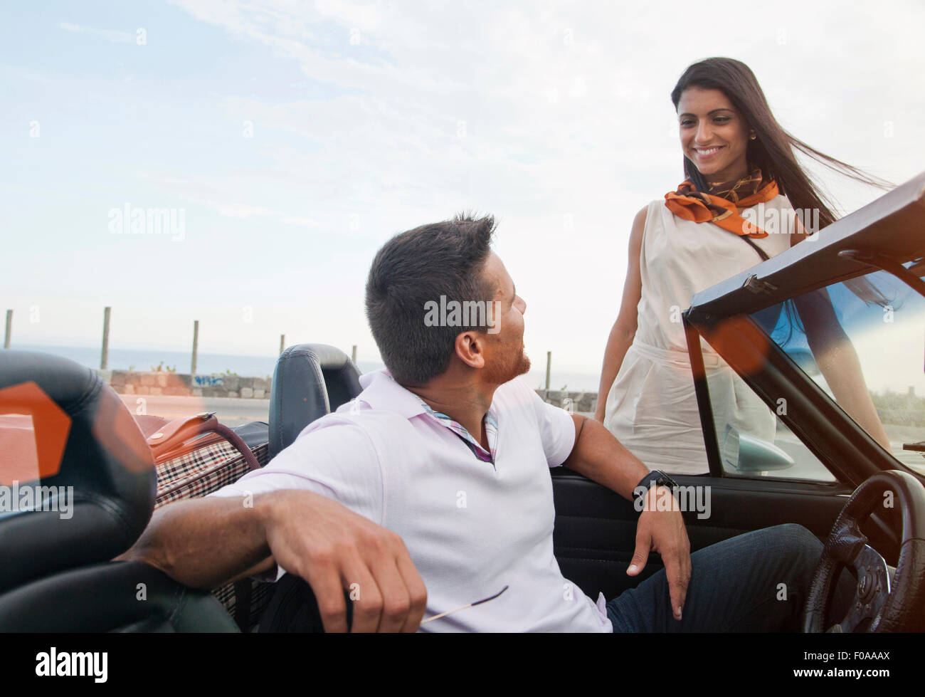 L'homme en voiture décapotable, femme debout à côté de voiture, smiling Banque D'Images