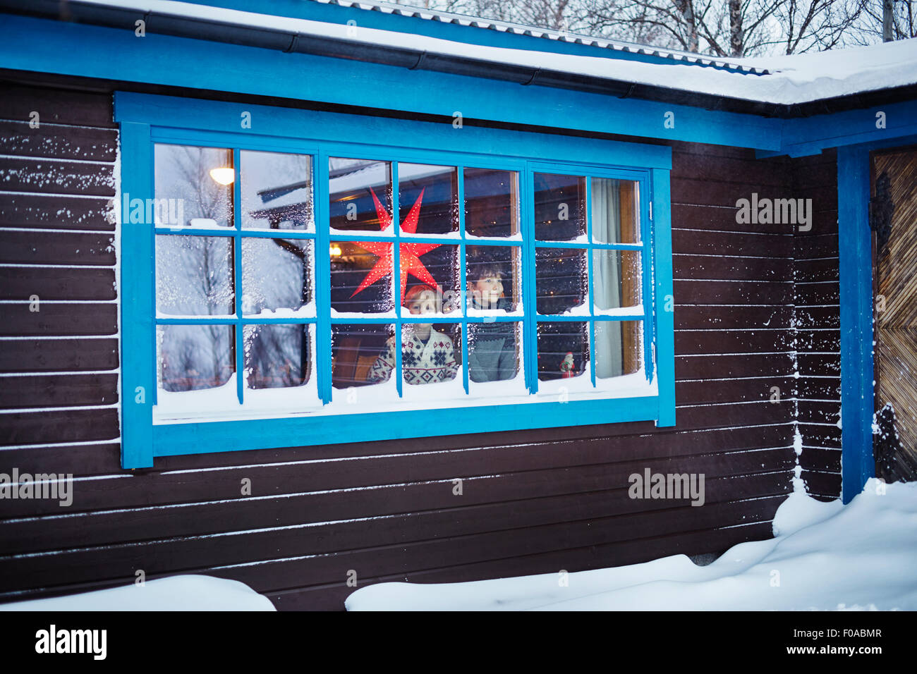 Deux frères à la recherche hors de la fenêtre de cabine couverte de neige à Noël Banque D'Images