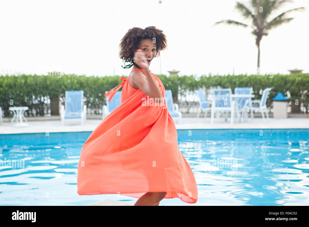 Portrait de jeune femme en robe orange virevoltante à la piscine de l'hôtel, Rio de Janeiro, Brésil Banque D'Images