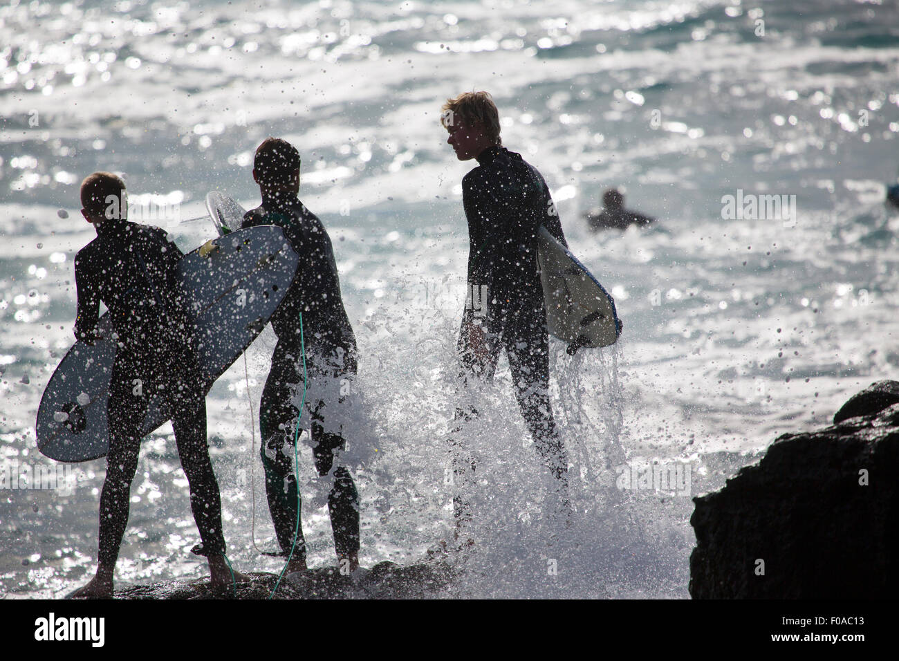 Trois hommes debout sur surfers silhouetted rochers marins, Fuerteventura, Espagne Banque D'Images