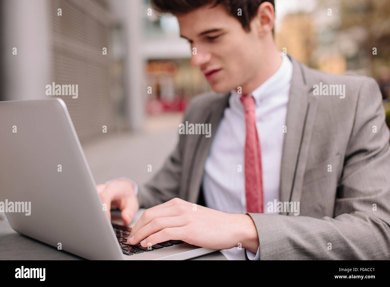 Ville jeune businessman typing on laptop at sidewalk cafe Banque D'Images