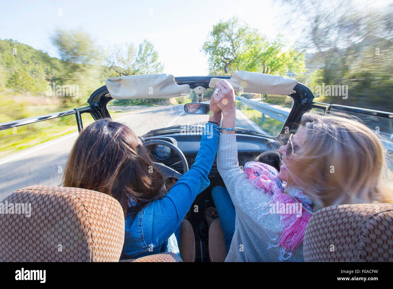 Deux femmes mûres, tenant les mains, en voiture décapotable, vue arrière Banque D'Images