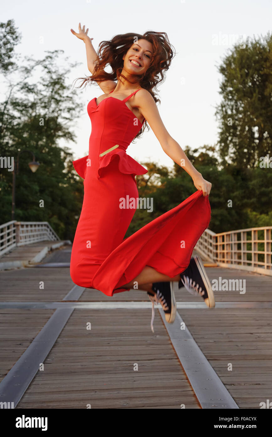 Portrait d'une jeune femme en robe rouge et smart chaussures de baseball en mouvement de saut Banque D'Images