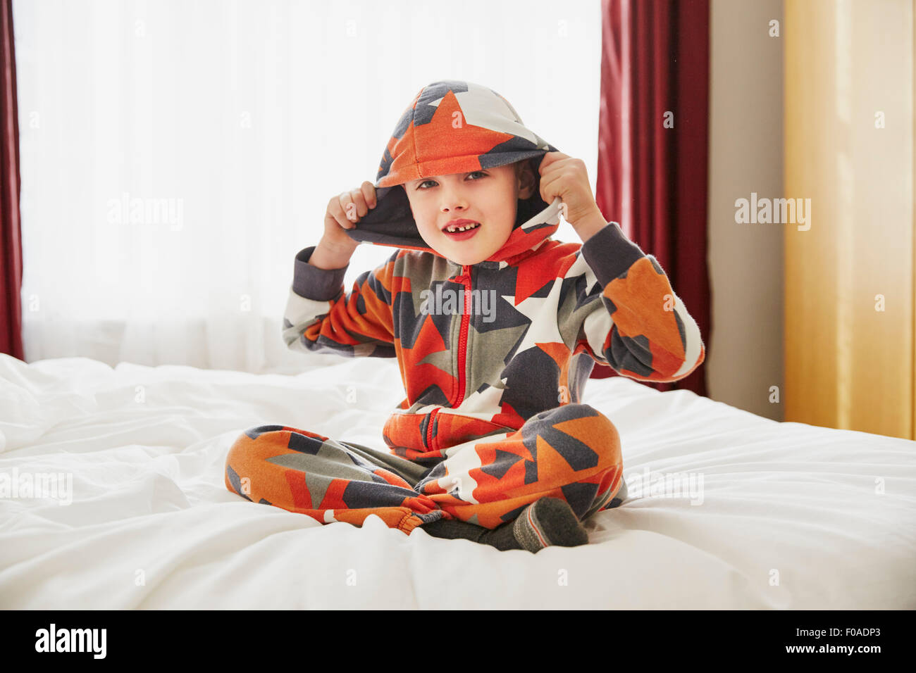 Young boy sitting on bed wearing hooded top Banque D'Images