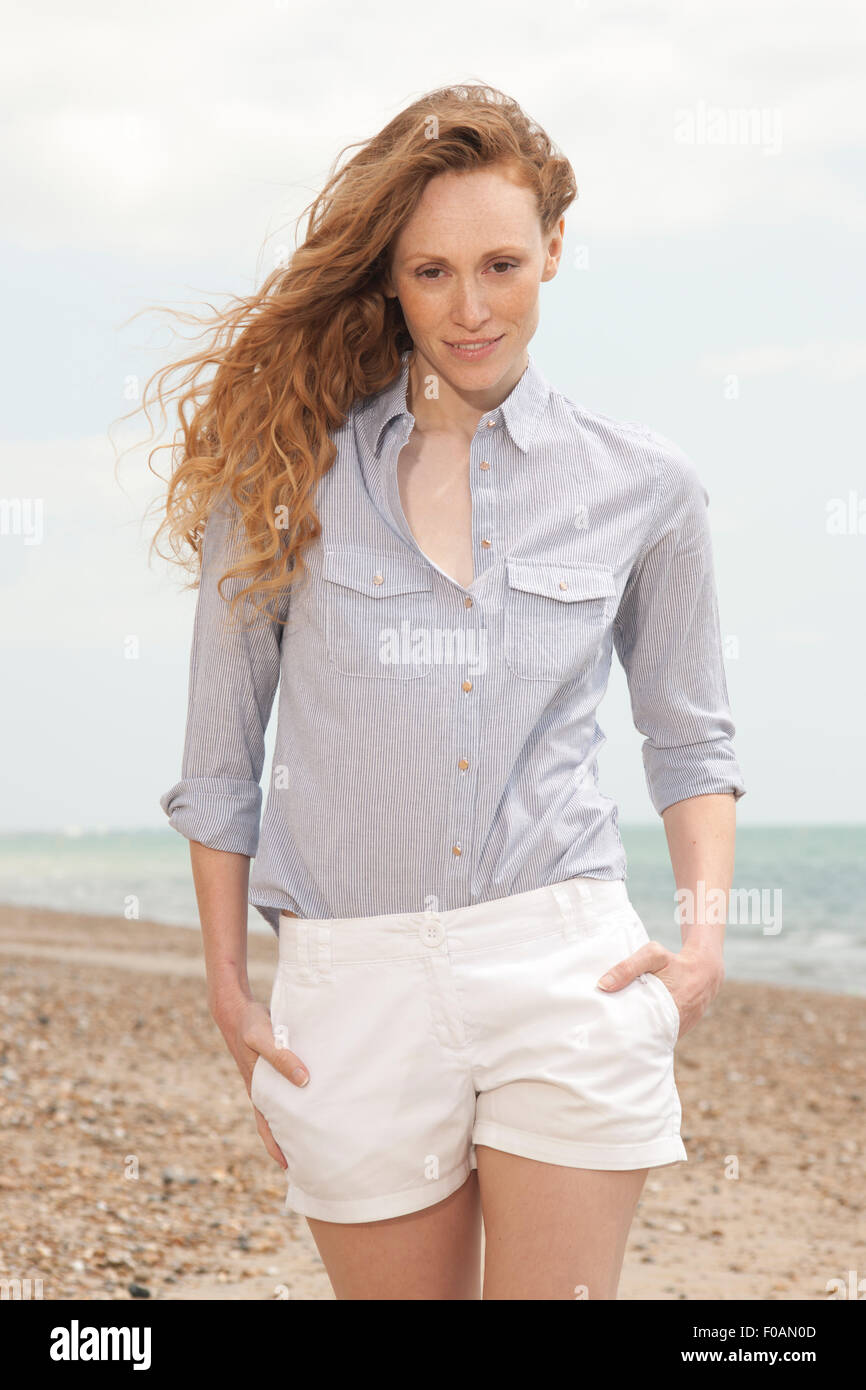 Jolie rousse femme marchant le long de la plage en short et maillot , les mains dans les poches. Banque D'Images
