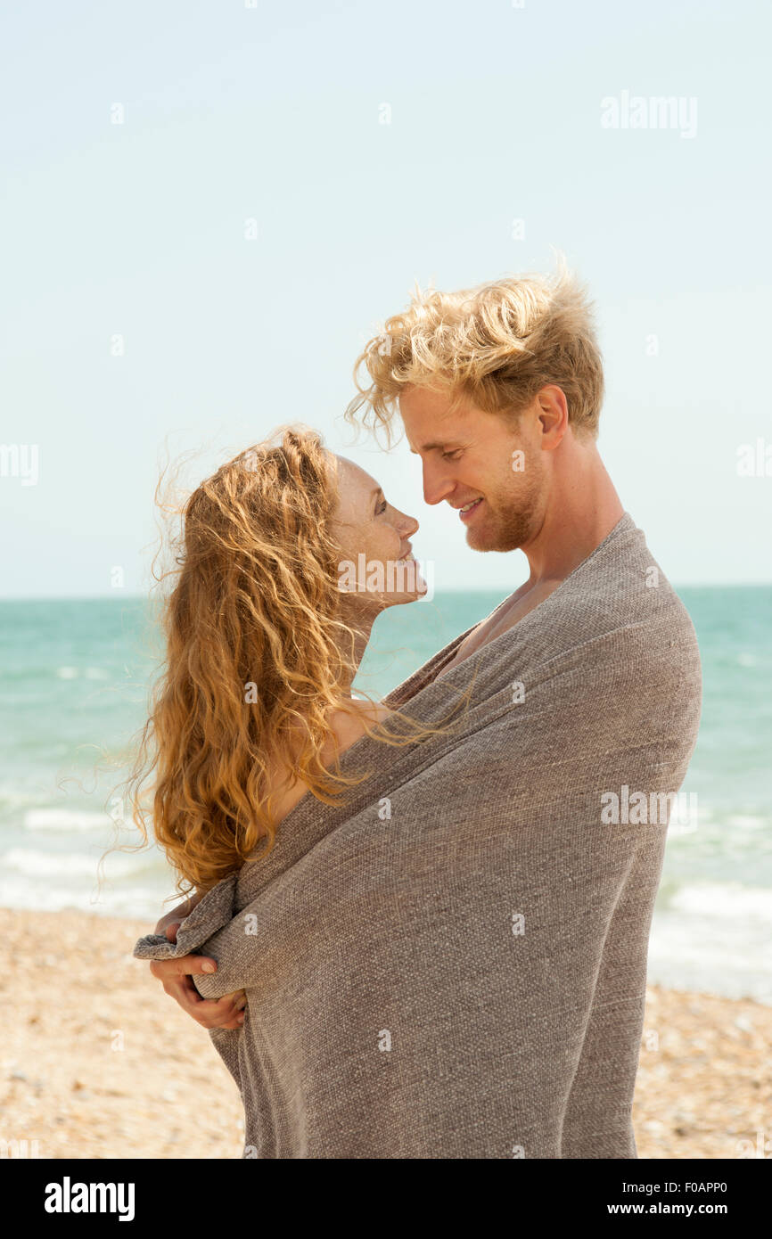 Romantic couple enveloppé dans une couverture à la plage après la baignade Banque D'Images