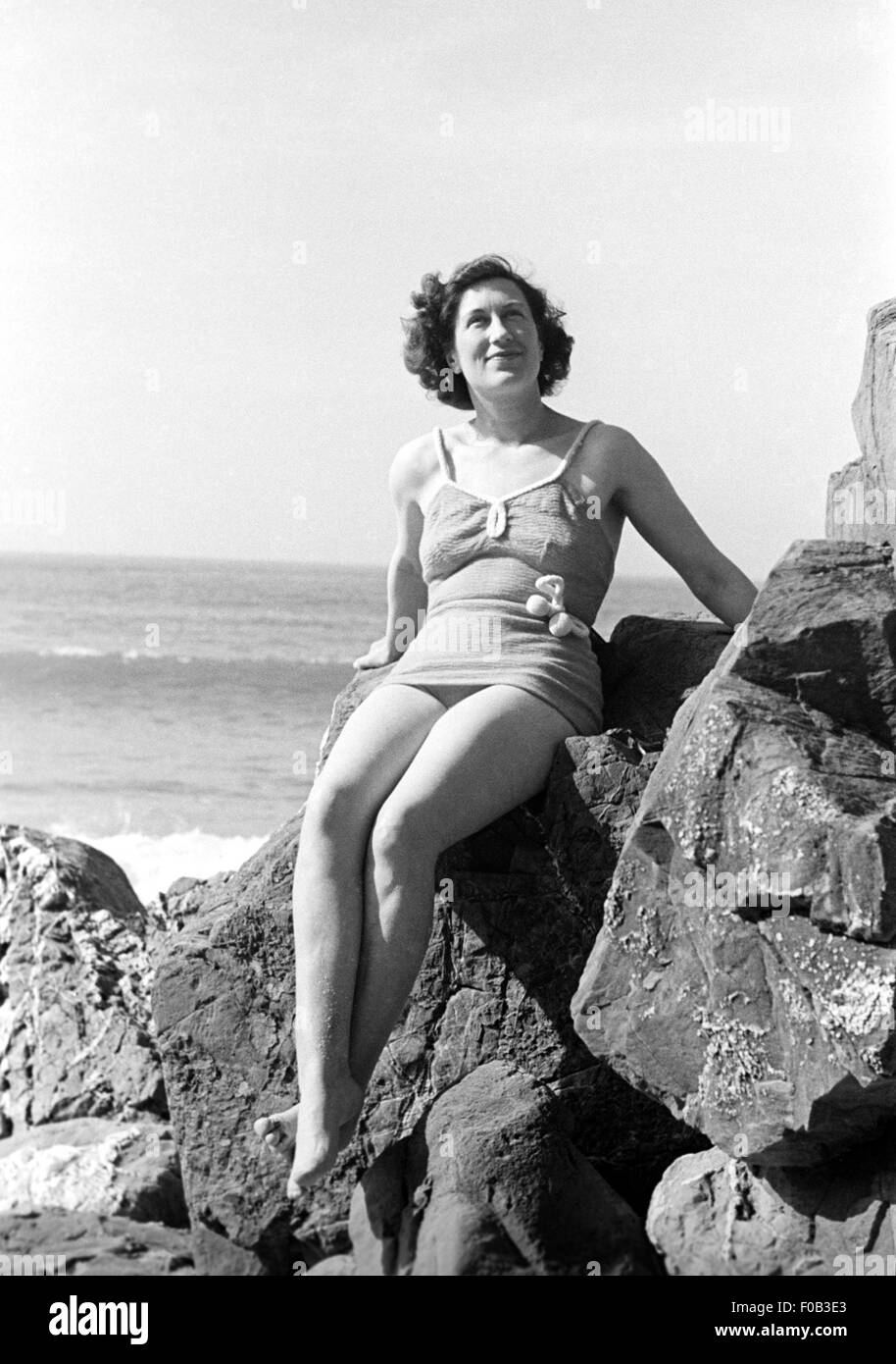 Une femme assise sur des rochers sur une plage Banque D'Images