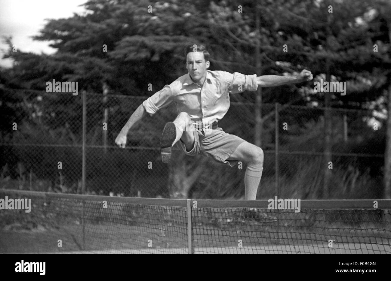 Un jeune homme sautant par dessus le filet en travers d'un court de tennis. Banque D'Images