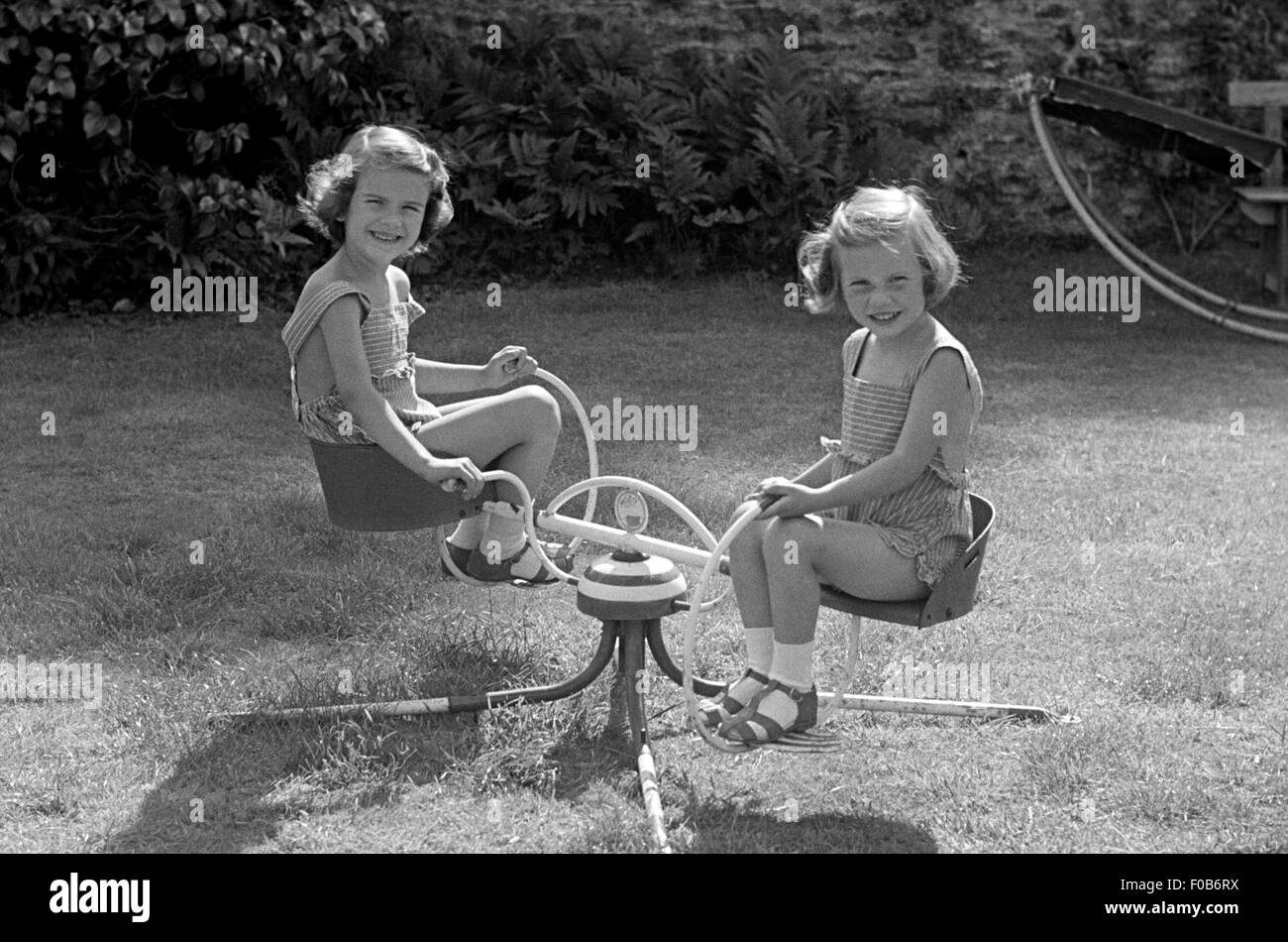 Deux jeunes filles portant des shorts pinafore jouant sur un manège dans le jardin. Banque D'Images