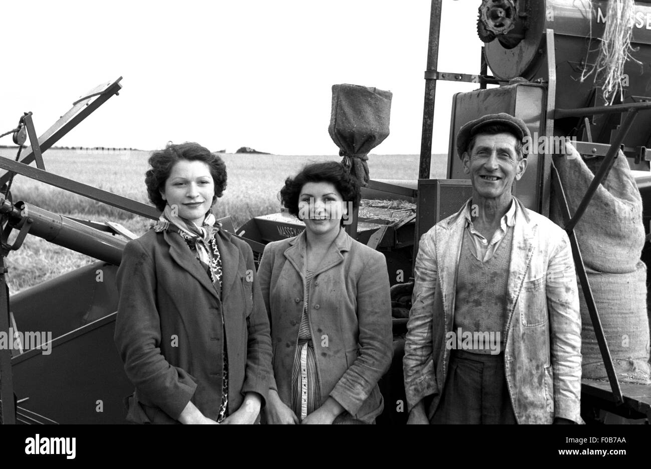 Un homme d'âge moyen et deux femmes debout à côté d'une moissonneuse-batteuse dans un champ de blé. Banque D'Images