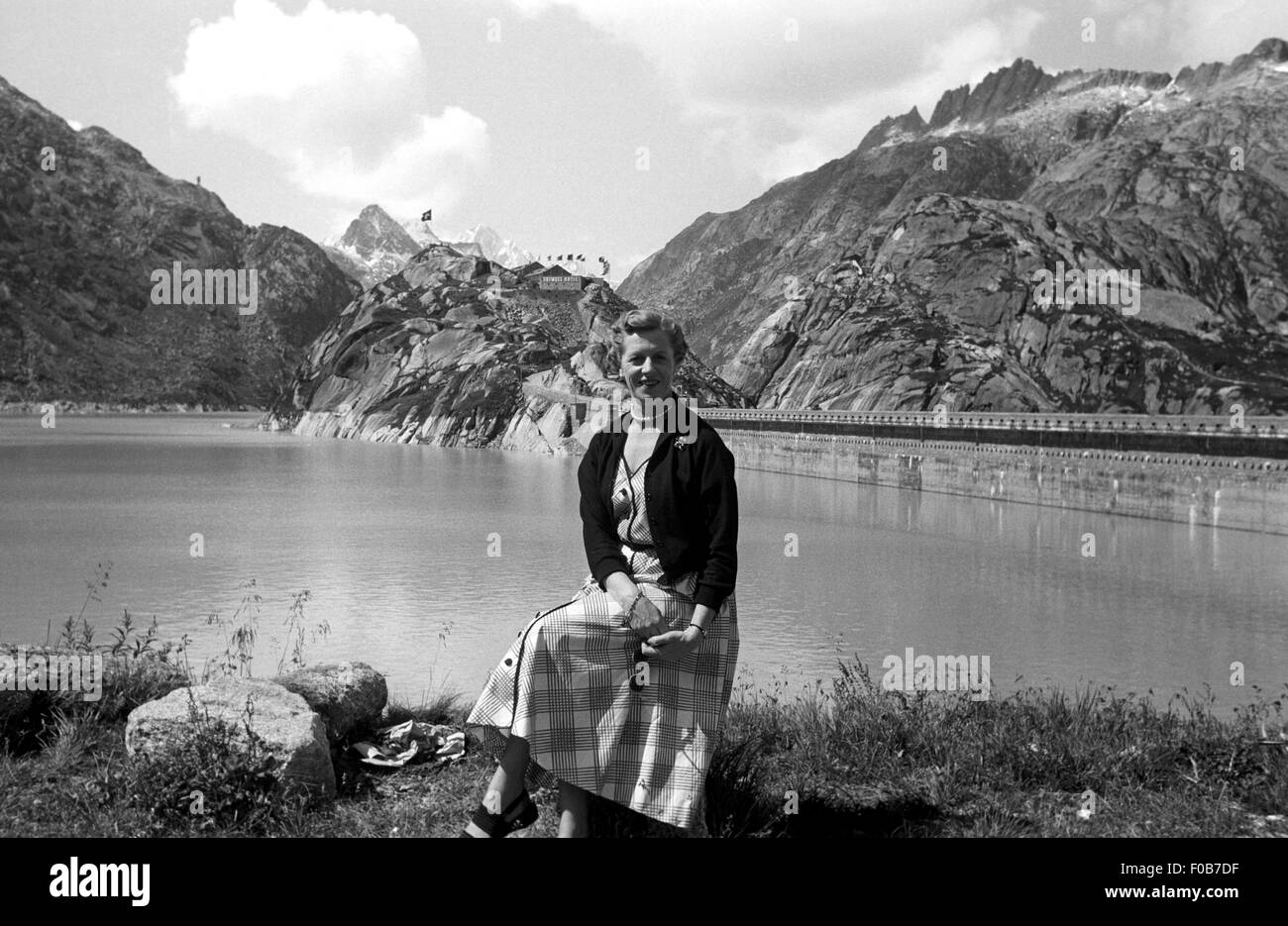 Une femme d'âge moyen assis sur les rives du lac de Grimsel avec un barrage dans l'arrière-plan, Suisse Banque D'Images