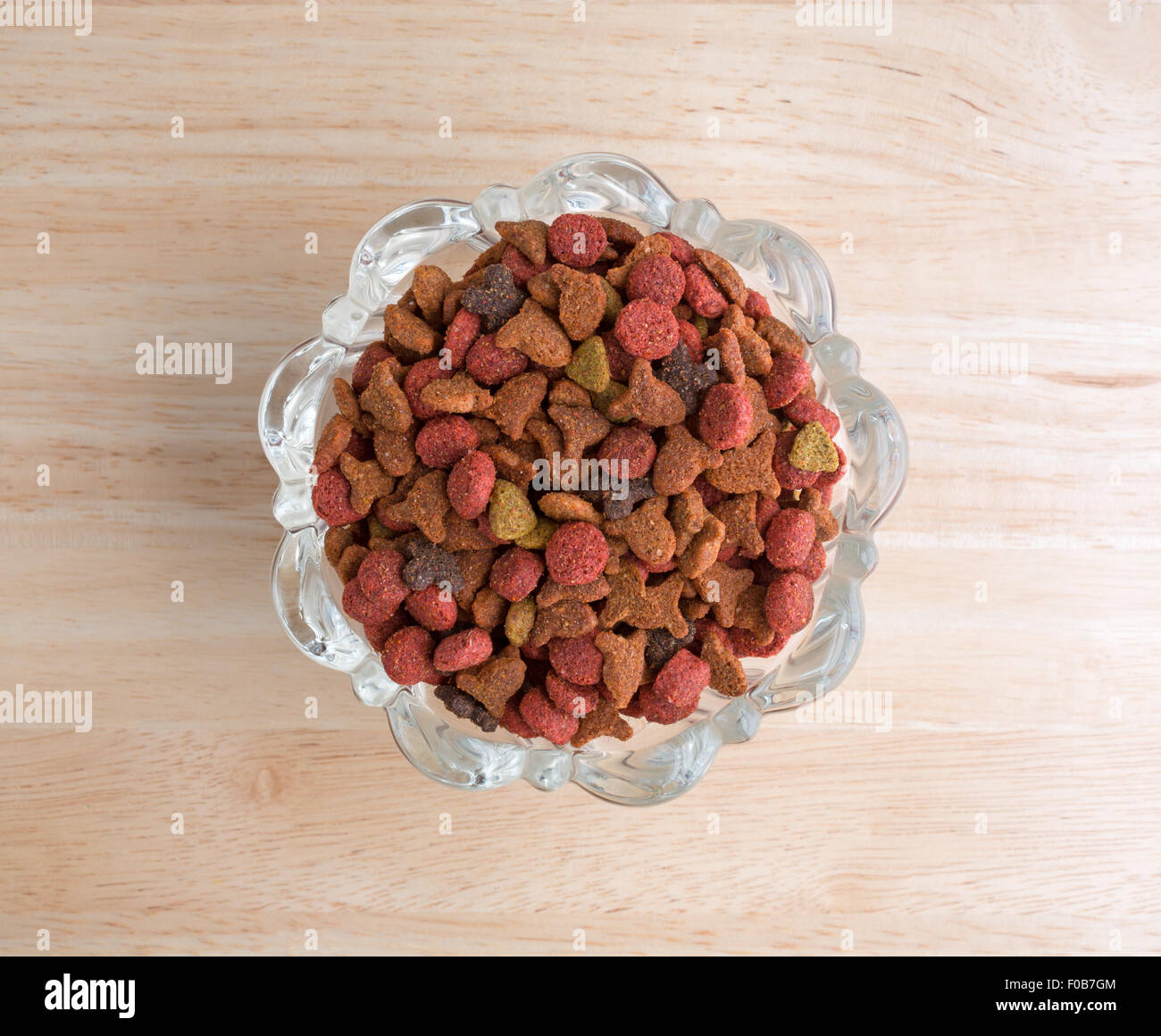 Vue de dessus d'un bol en verre décoratif rempli d'aliments secs pour chats générique sur un comptoir en bois. Banque D'Images