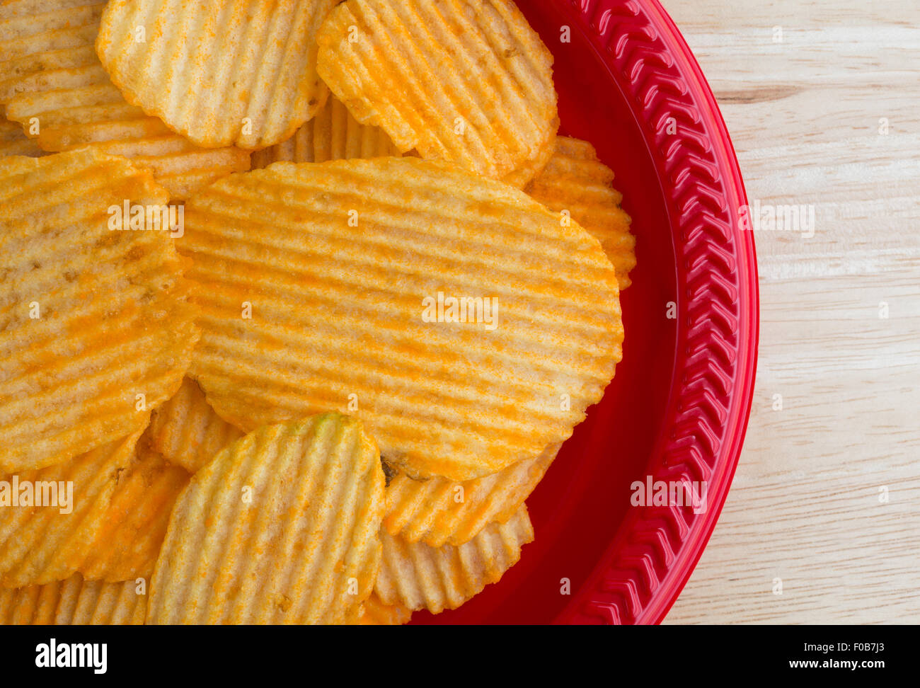 Haut de page Fermer la vue de fromage cheddar saveur de croustilles de pommes de terre sur un plat en plastique rouge en haut d'une table en bois éclairé par la lumière naturelle. Banque D'Images