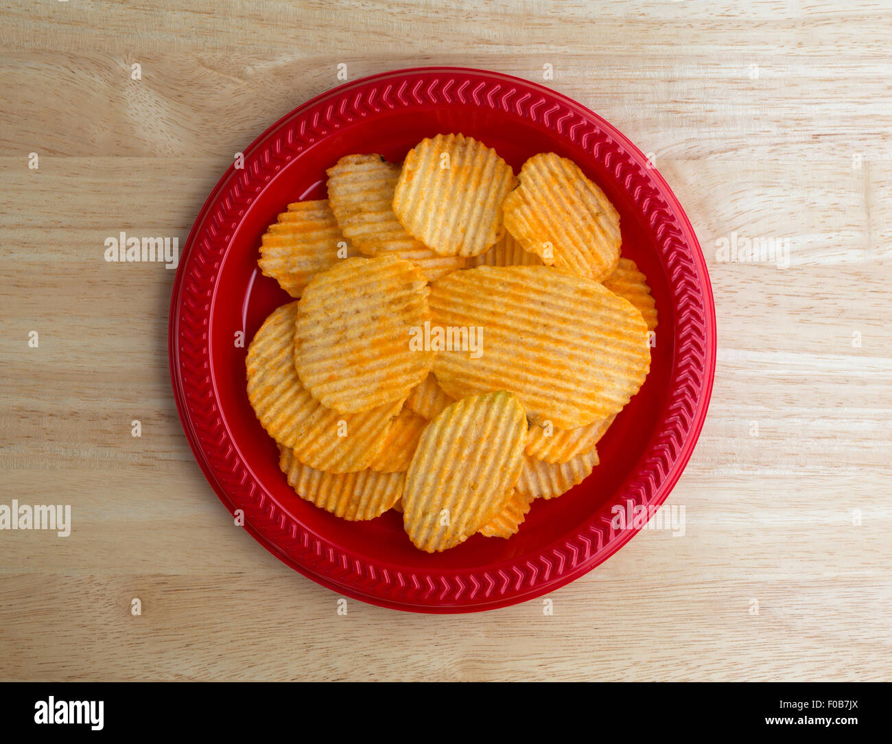 Vue de dessus d'une plaque en plastique rouge avec une portion de fromage cheddar saveur de croustilles de pommes de terre sur une table en bois Banque D'Images