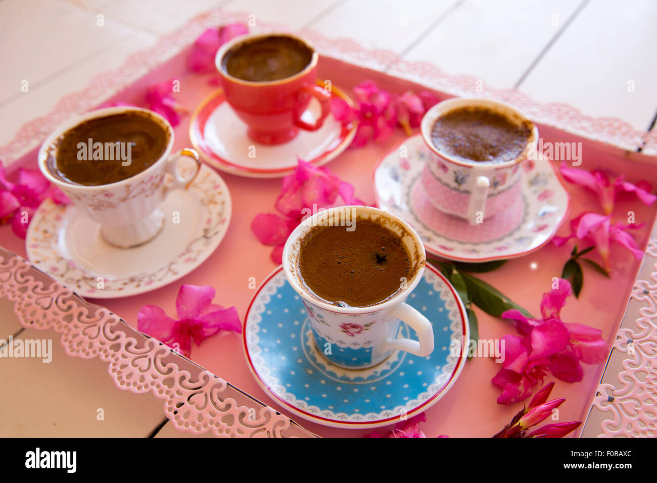 Quatre petites tasses de café turc mousseux traditionnel servant sur un plateau rose à fleurs colorées sur le dessus d'une table en bois blanc, dans la région de lo Banque D'Images