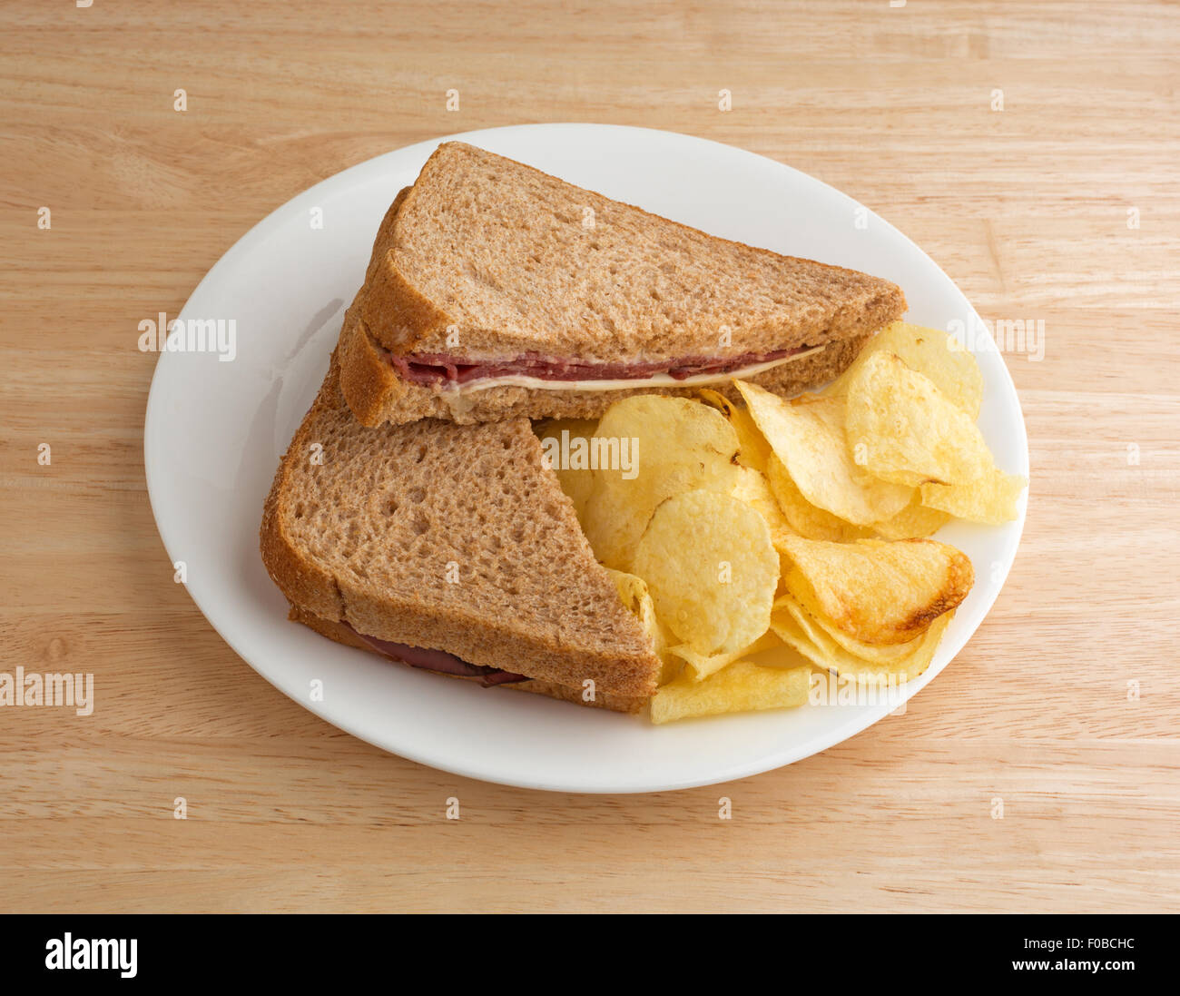 Un pain de blé rôti de bœuf sandwich avec du fromage blanc et la mayonnaise et croustilles de pommes de terre sur une plaque blanche au sommet d'une table en bois. Banque D'Images