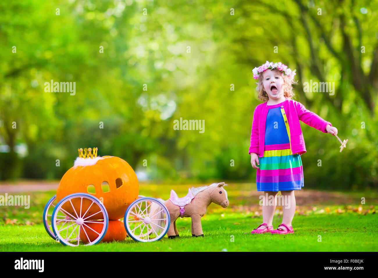 Cute little girl playing bouclés conte Cendrillon holding baguette magique à côté d'un chariot de citrouille en automne park à l'Halloween. Banque D'Images