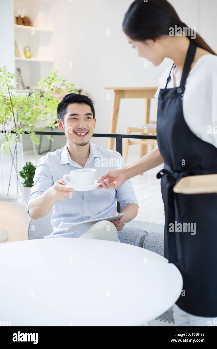 Jeune homme waitress une tasse de café Banque D'Images