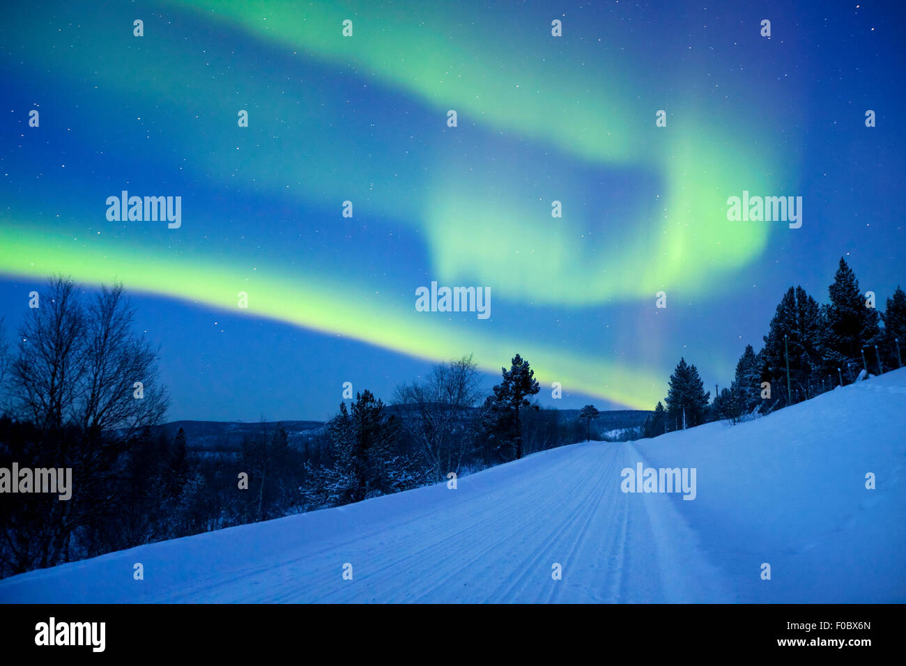 Des aurores boréales au-dessus d'une route à travers un paysage d'hiver en Laponie finlandaise. Banque D'Images